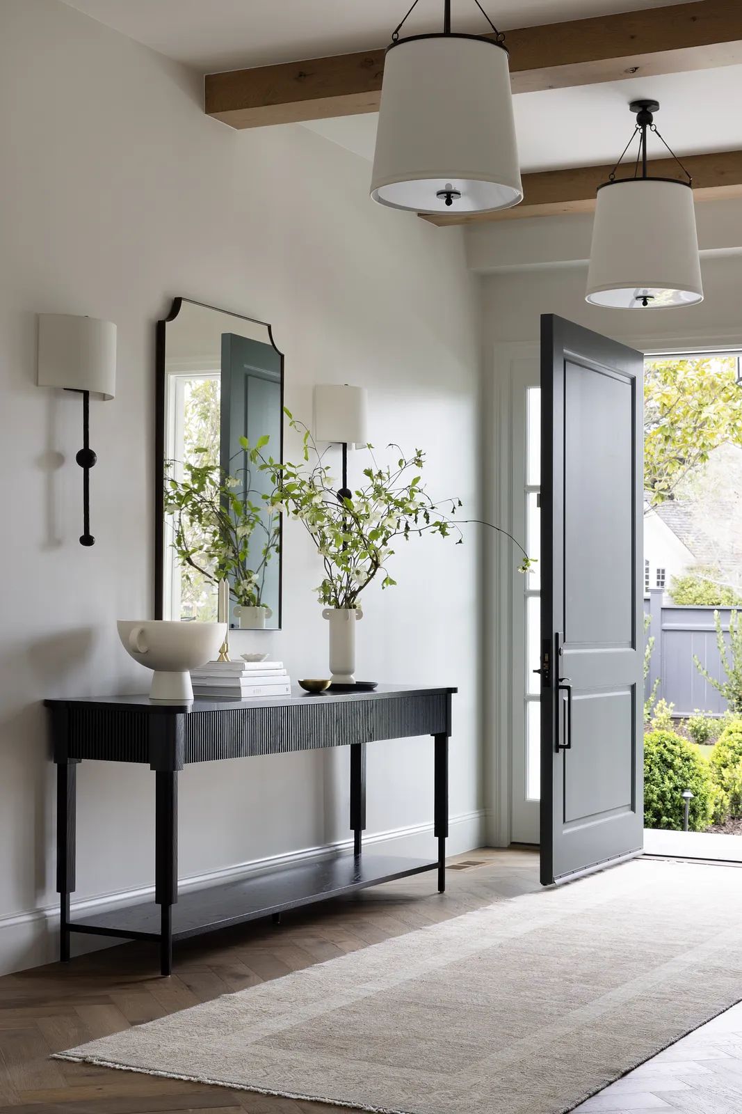 Foyer with black console table, mirror, sconces, vase, and large door providing natural light