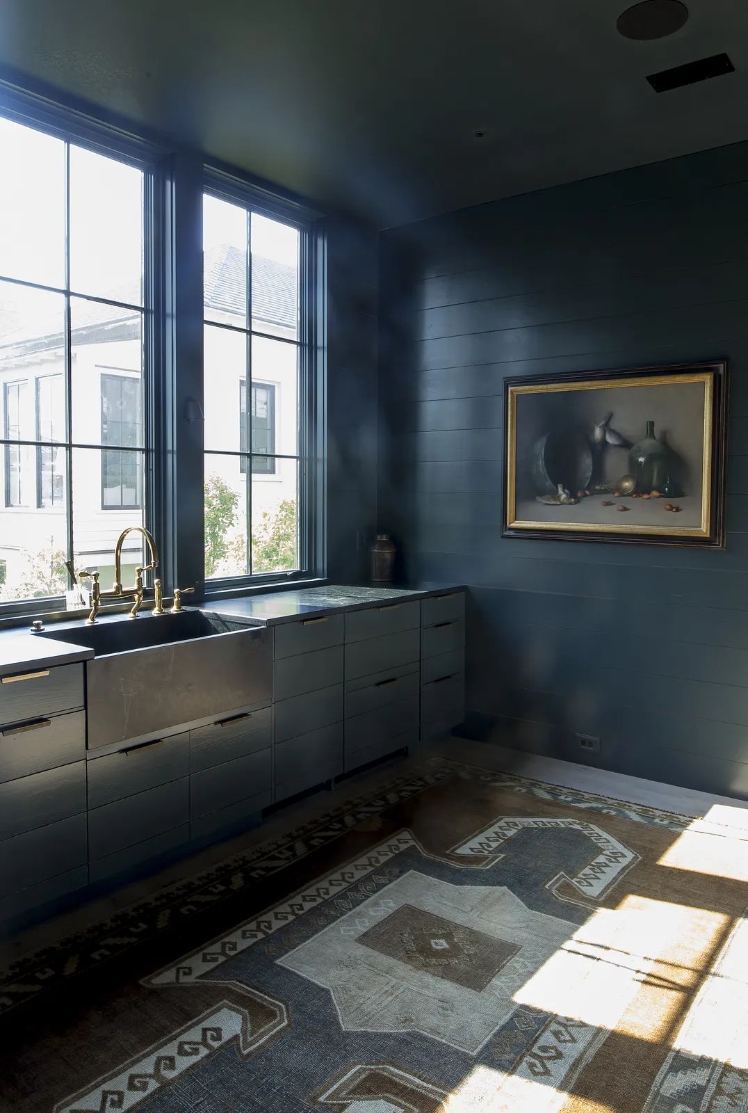 Kitchen with dark blue walls, farmhouse sink, brass faucet, wooden cabinet, and patterned rug.
