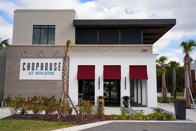 Commercial exterior with glass doors, red awnings, light brick, plants, and 'Chophouse at Nocatee' sign.