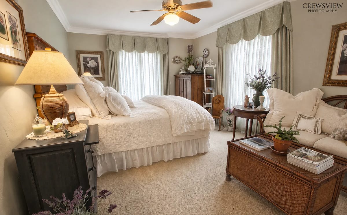 Bedroom with queen bed, windows, lamp, armoire, sofa, and decorative shelving.
