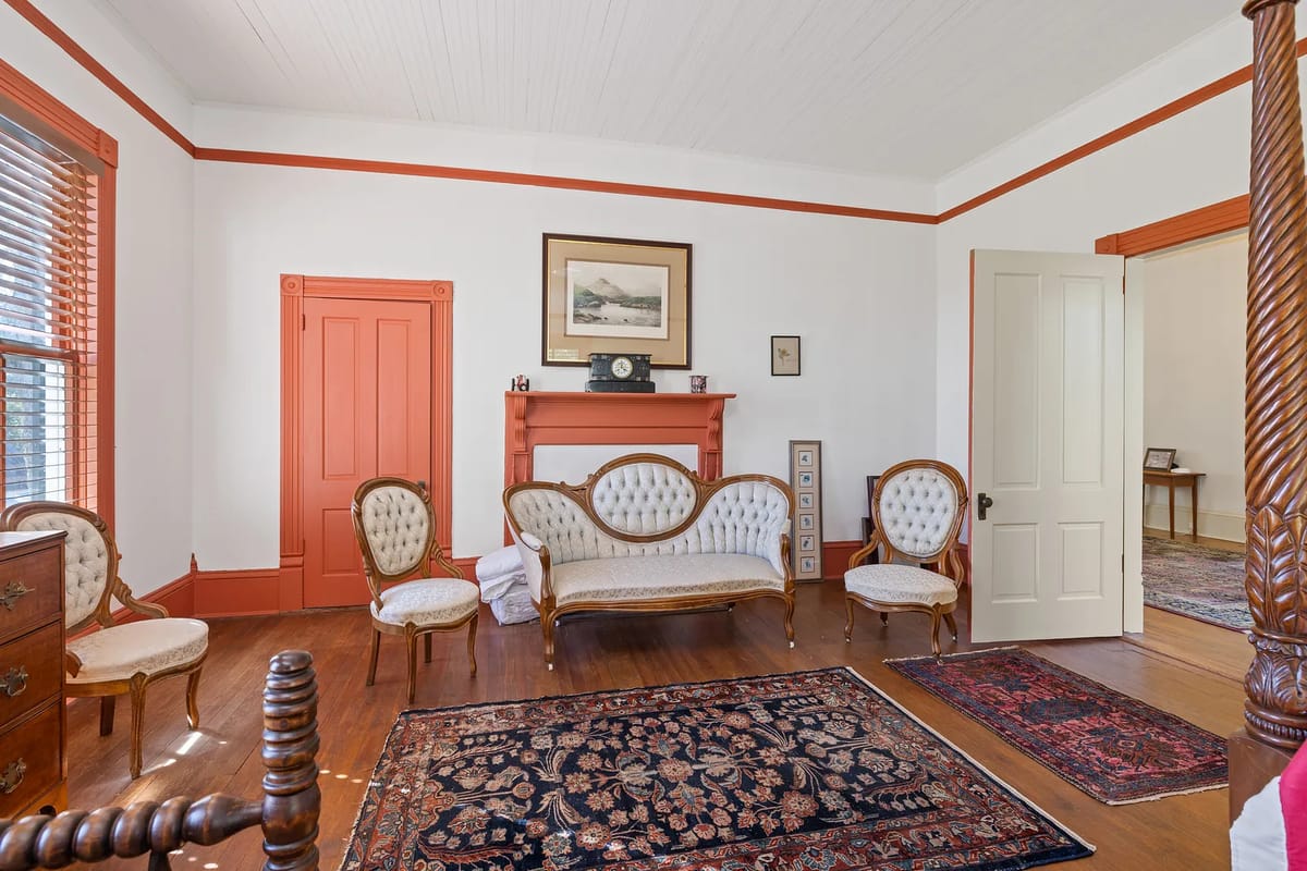 Living room with vintage sofa, upholstered chairs, decorative rugs, and wooden floors with orange trim.