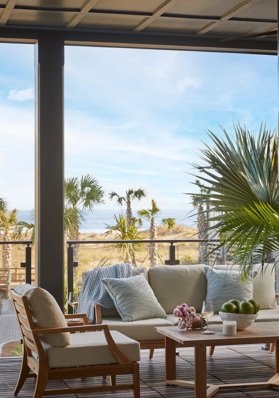 Patio with light-colored sofa, wooden armchair, coffee table, and a view of palm trees.