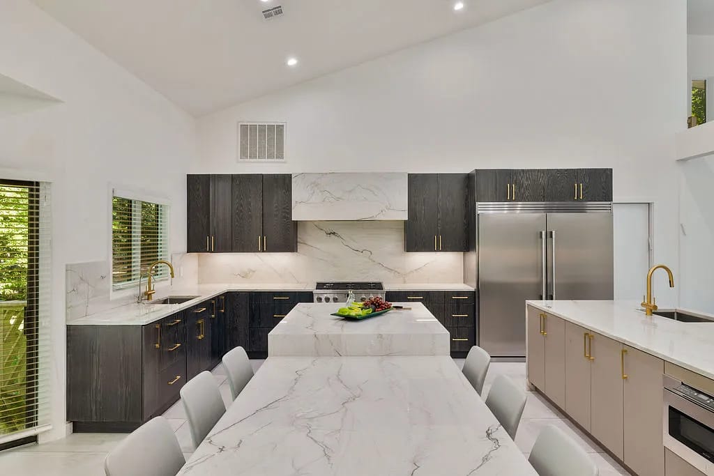 Kitchen with dark wood cabinets, marble countertops, island with stools, and stainless steel appliances.