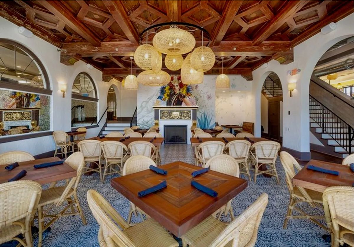 Dining room with wooden tables, wicker chairs, coffered ceiling, arched windows, and decorative fireplace.