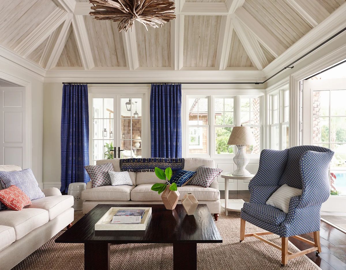 Living room with light sofa, dark wood coffee table, area rug, blue drapes, and patterned accent chair.