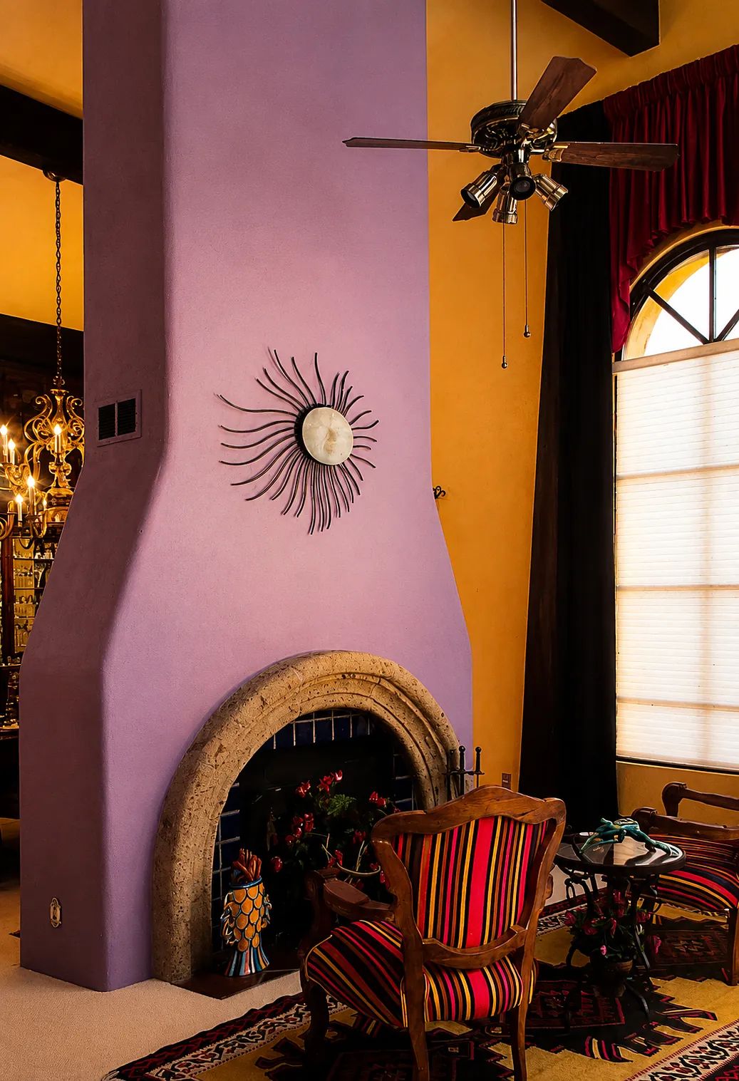Living room with purple chimney, armchair, coffee table, patterned rug, red curtains, and chandelier.