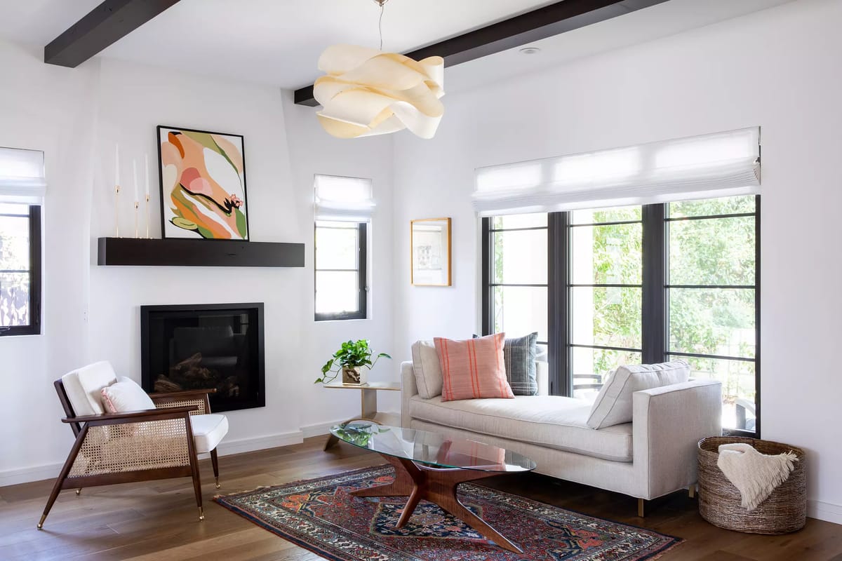 Living room with white sofa, wood coffee table, area rug, fireplace, large windows, and artwork.