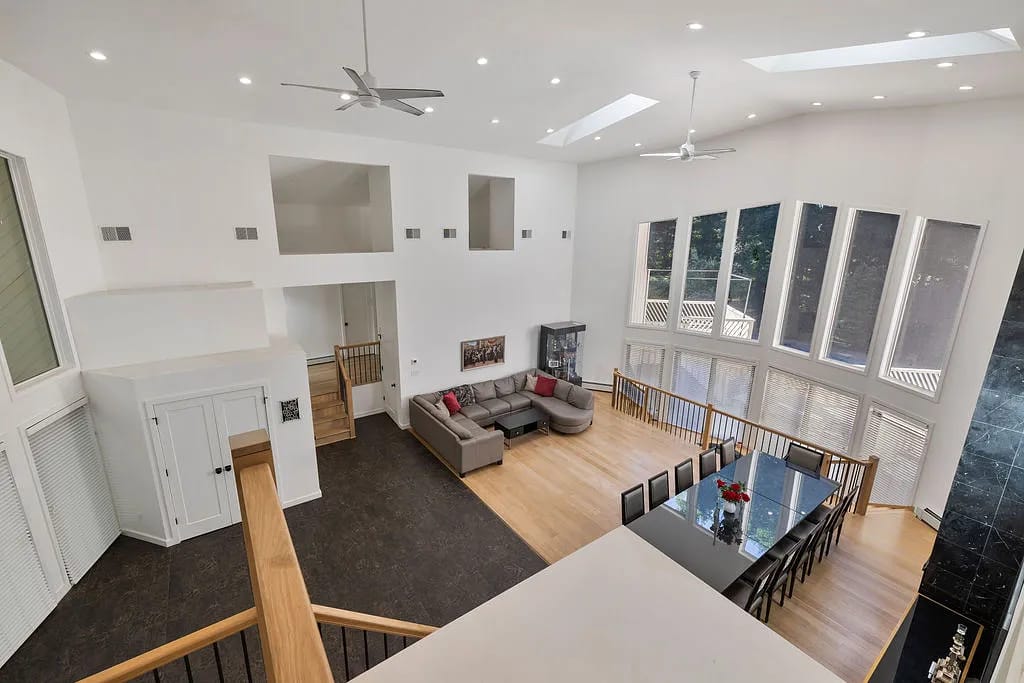 Open living room and dining area with gray sectional sofa, black dining table, wooden chairs, and large windows.