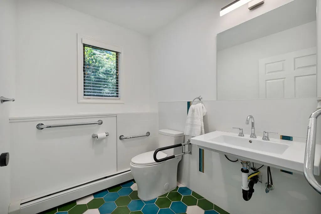 Bathroom with white toilet, wall-mounted sink, hexagonal blue and green tiles, and a small window
