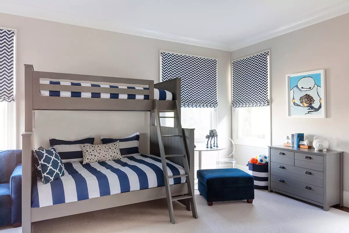 Bedroom with bunk bed, blue ottoman, gray dresser, patterned blinds, and light carpet.