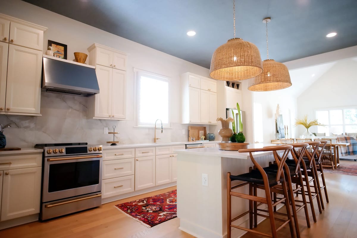 Kitchen with white cabinets, stainless steel range, marble backsplash, island with bar stools, and decorative items.