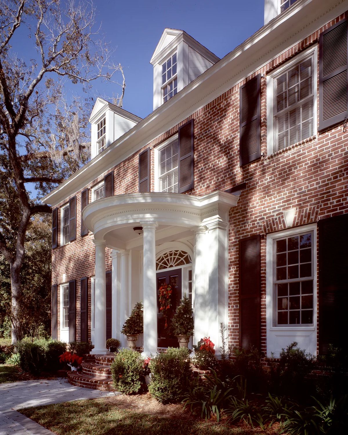 Front exterior with brick façade, white columns, multiple windows, and landscaped garden