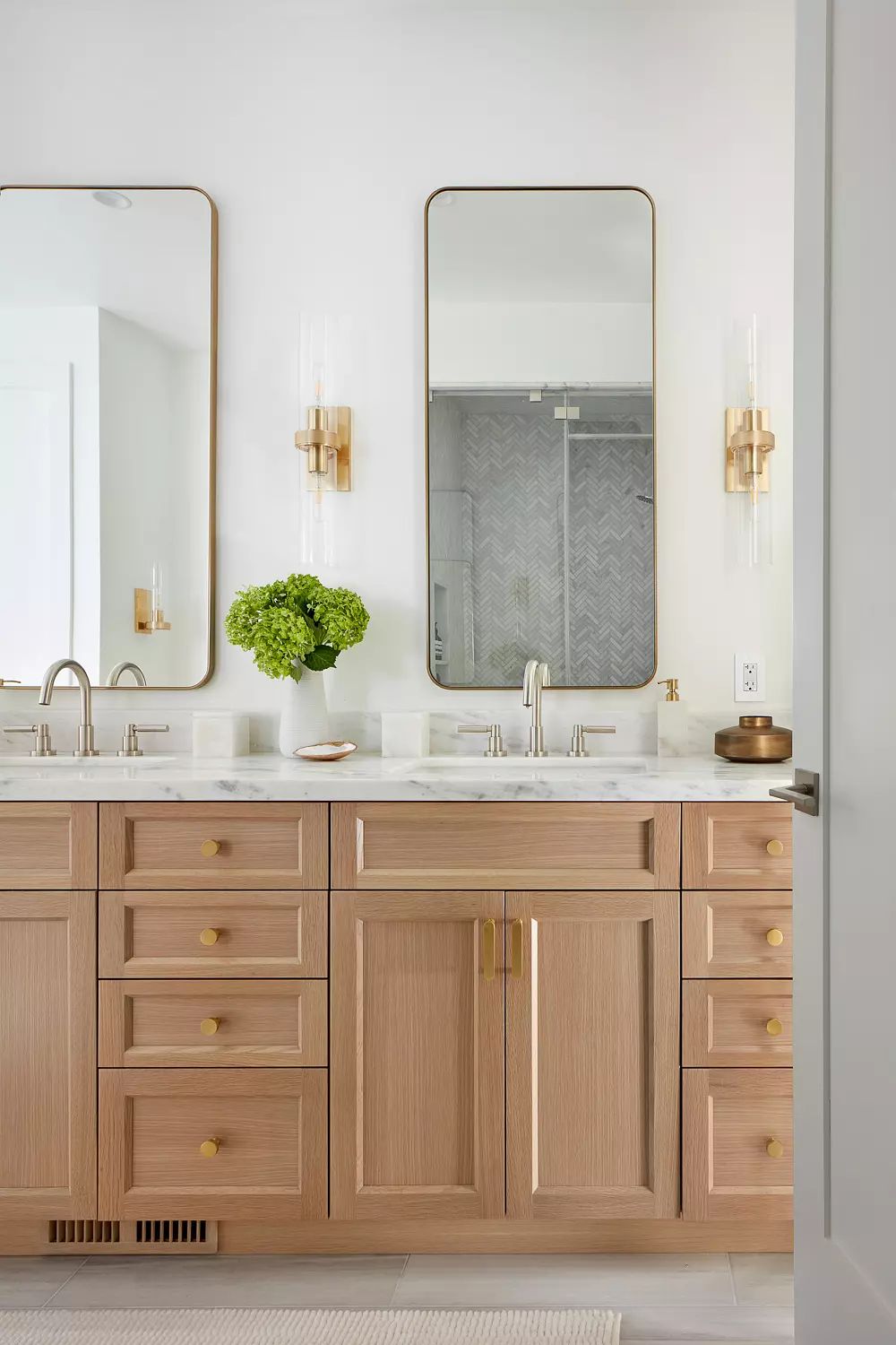 Bathroom with dual sink vanity, marble countertop, mirrors, wall sconces, and chevron tile shower.