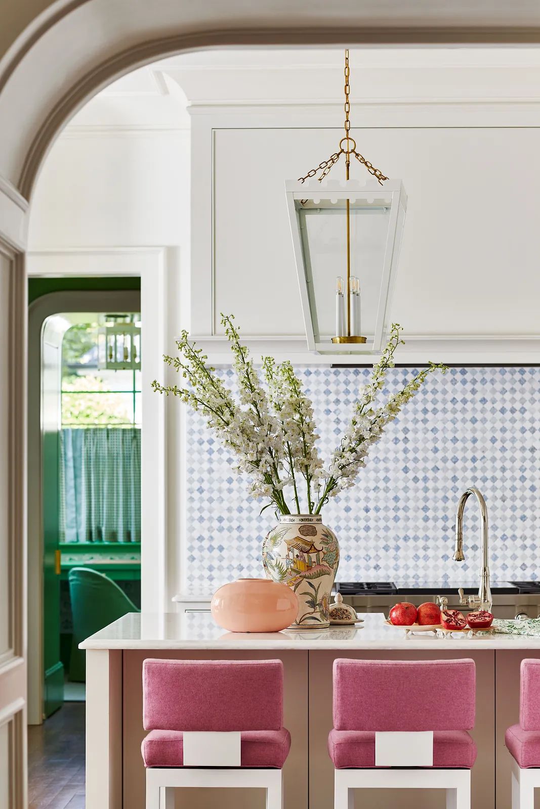 Kitchen with island, pink bar stools, flowers, blue-patterned backsplash, and green seating.