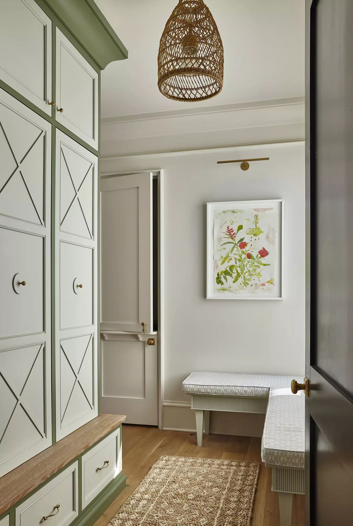 Mudroom with built-in cabinetry, wooden bench, artwork, woven pendant light, hooks, and a jute rug.