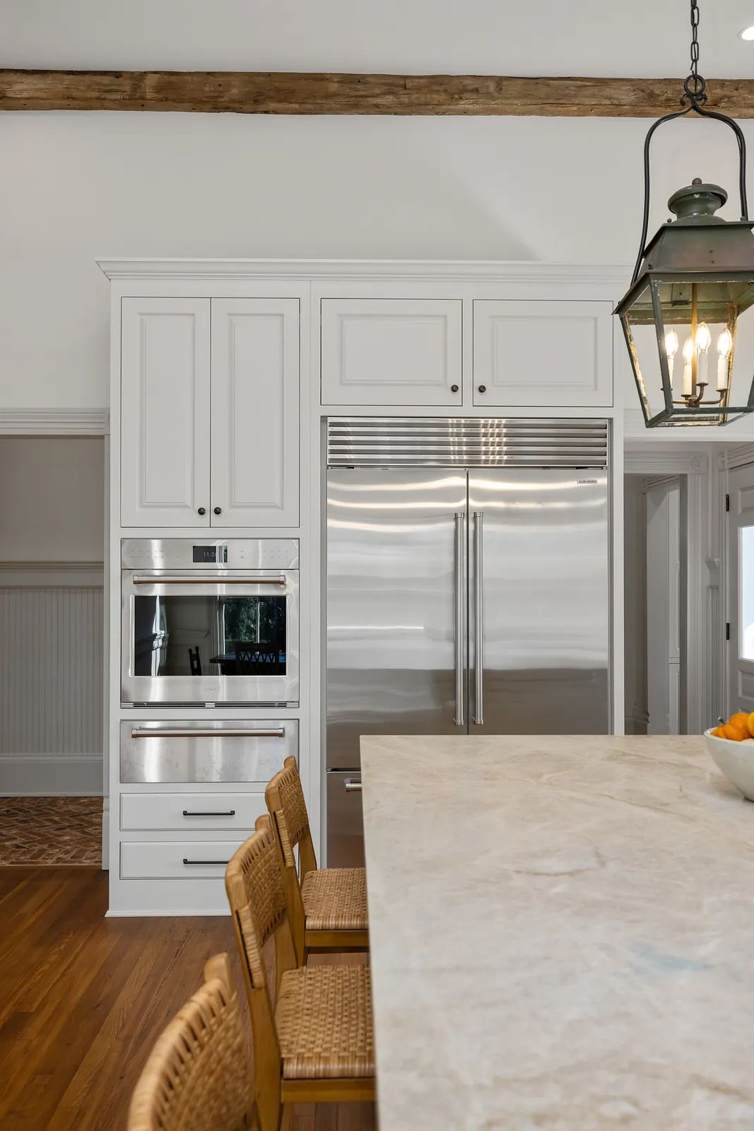 Kitchen with white cabinetry, stainless steel appliances, marble island, and woven seating.