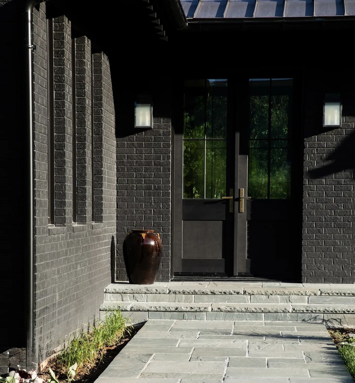 Exterior front view with dark brick, double door entrance, stone pathway, and ceramic vase.