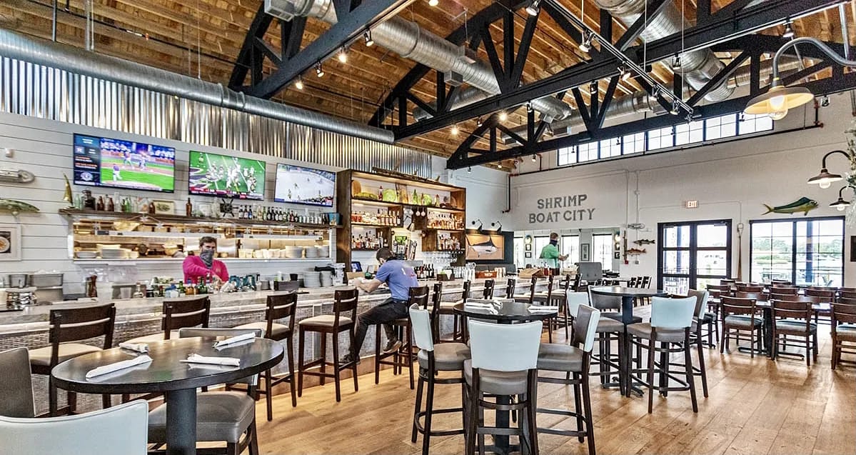 Dining room with bar area, high-top chairs, TV screens, wooden floors, and pendant lights.