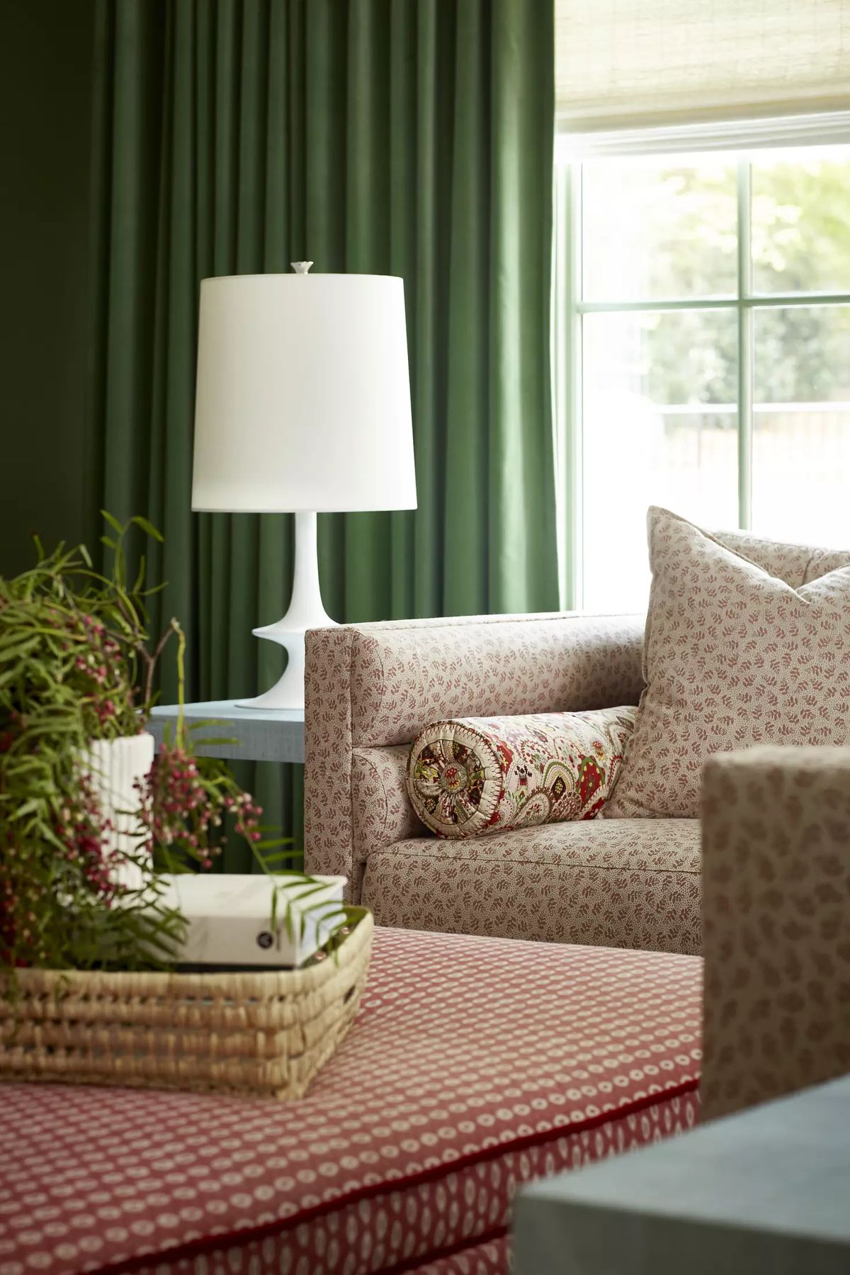 Living room with pink patterned sofa, green walls, round side table, and white lamp.