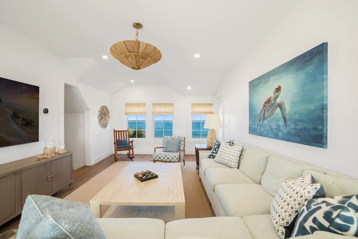Living room with sectional sofa, coffee table, area rug, large windows, side chair, and sea turtle painting.