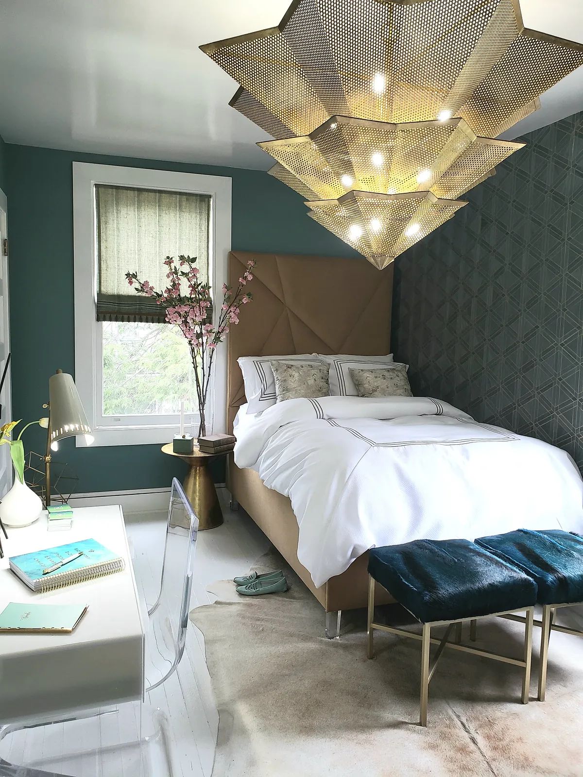 Bedroom with beige bed, white bedding, desk, clear chair, pink plant, and teal geometric walls.