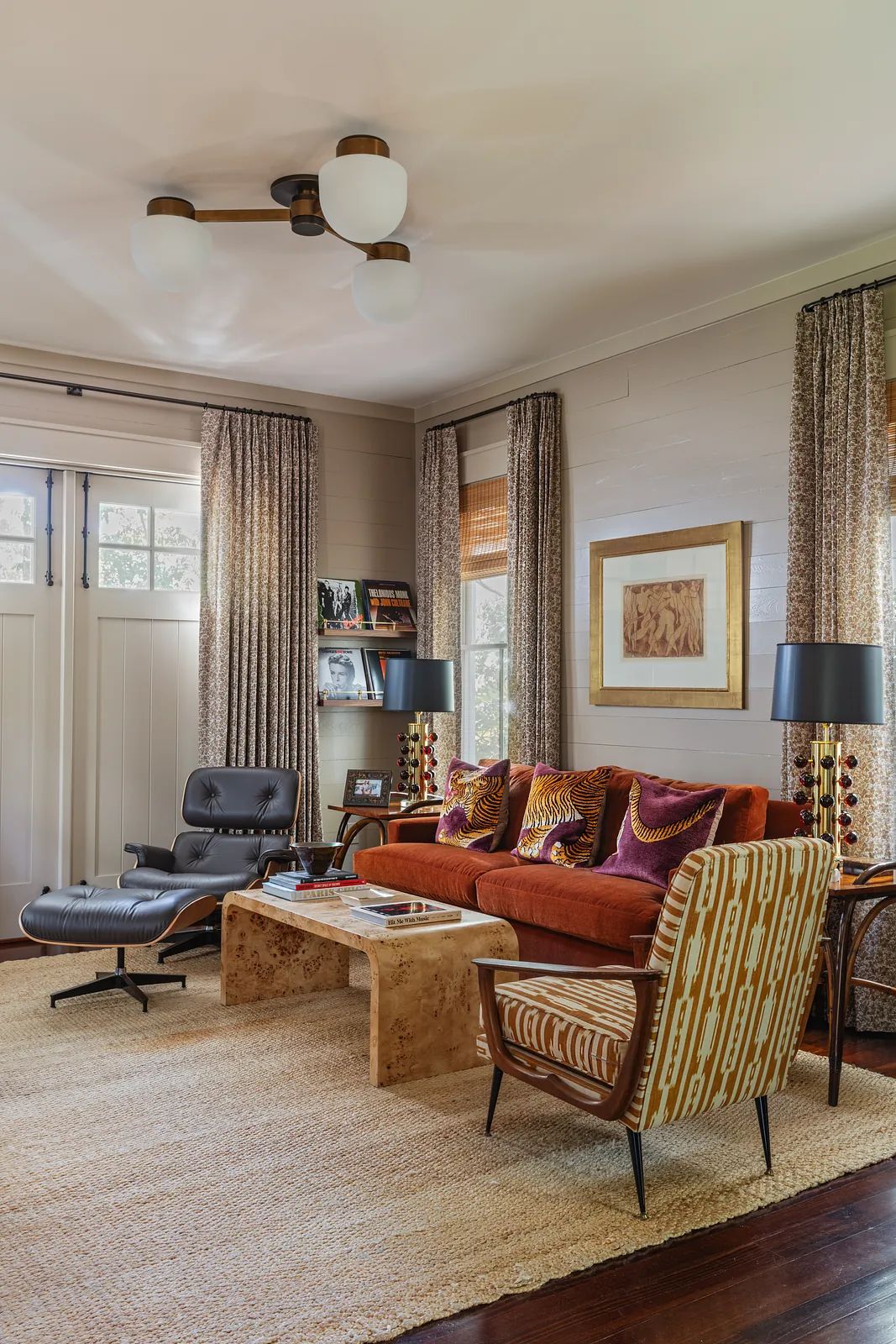 Living room with brown sofa, natural wood coffee table, two chairs, artwork, and hardwood floor with area rug.