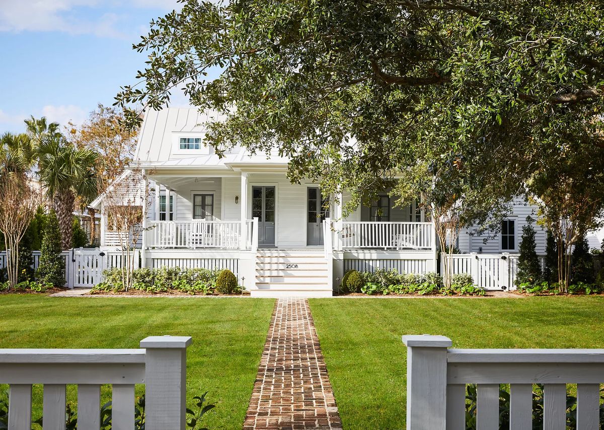 Exterior front view of a house with white facade, porch, brick pathway, and landscaping.