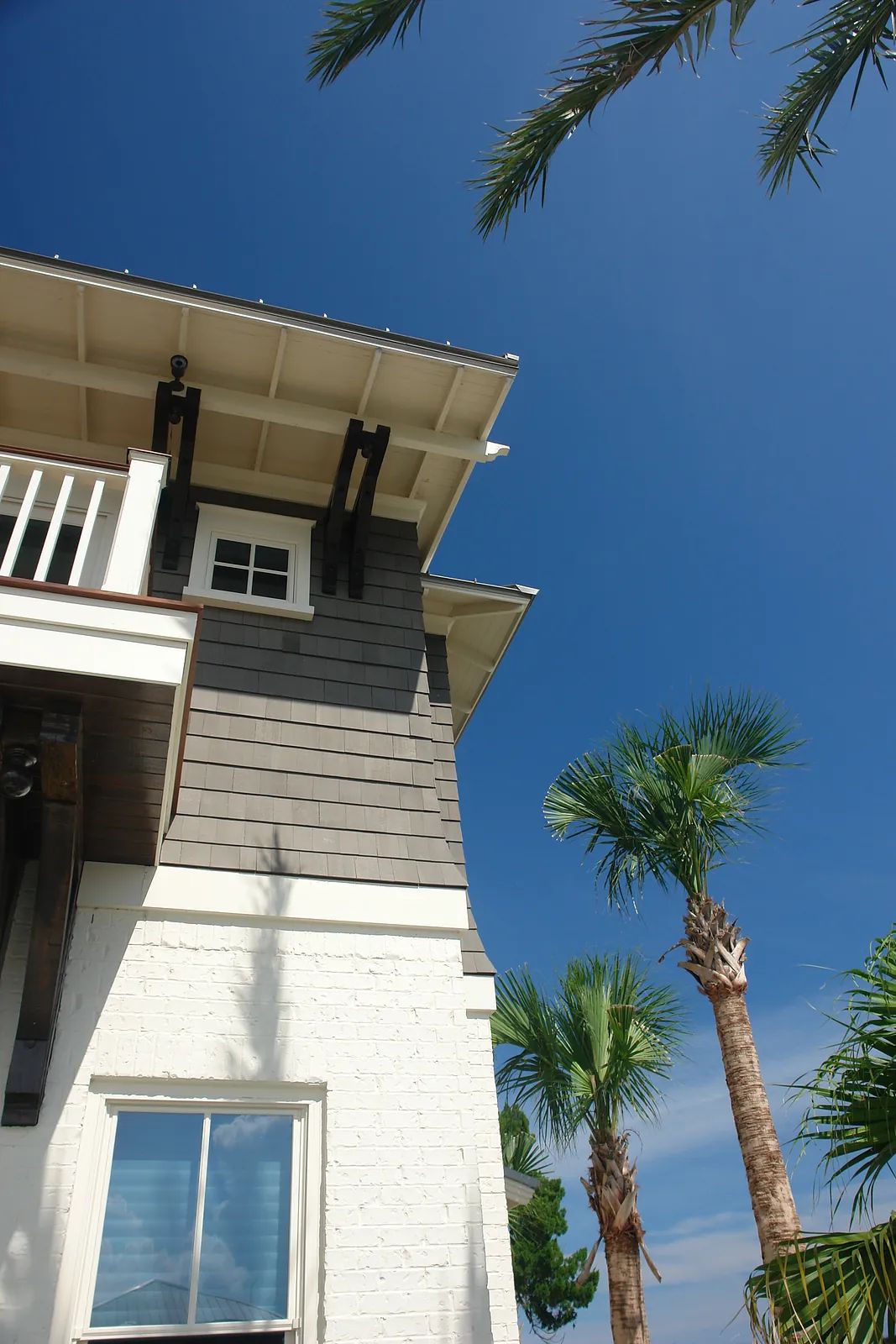 Exterior view of a two-story house with shingle siding, white brick, and palm trees.