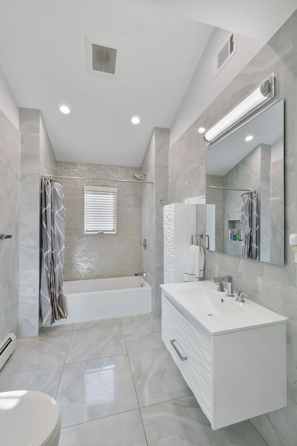 Bathroom with white vanity, large mirror, bathtub, shower area, gray tiles, and a decorative backsplash.