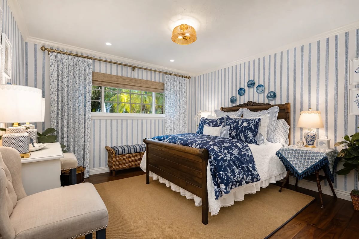 Bedroom with wooden bed, blue and white textiles, nightstand, dressing table, curtains, and blue-striped wallpaper