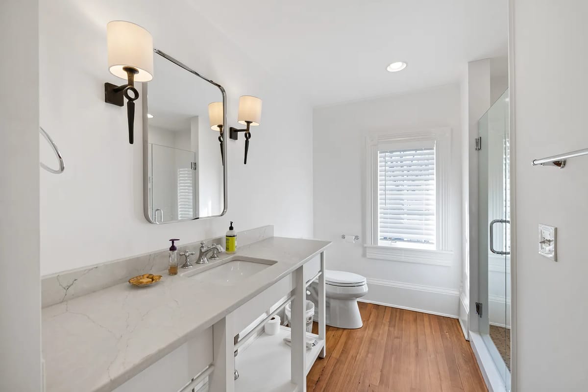 Bathroom with marble vanity, dual sinks, large mirror, toilet, and glass shower.