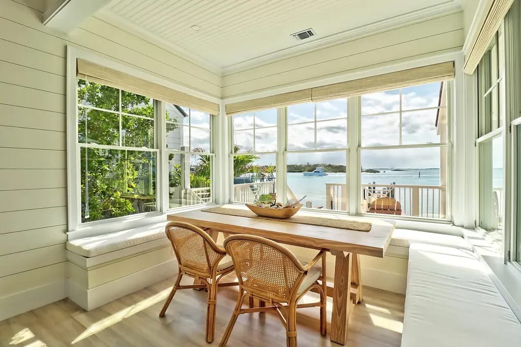 Dining room with wooden table, woven chairs, bench seating, and large windows with natural light.