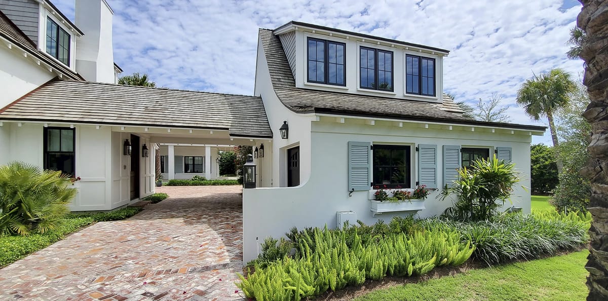 Exterior front view of a house with white facade, gray shingles, blue shutters, and landscaping with ferns.