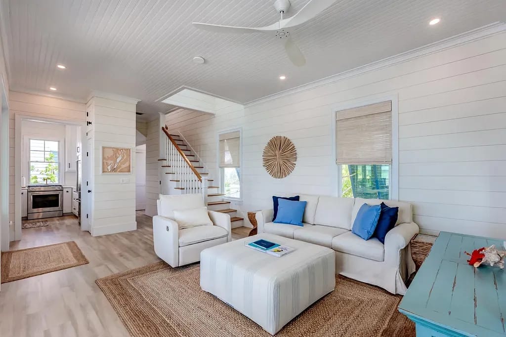 Living room with white sectional sofa, blue cushions, armchair, teal side table, and stairs.