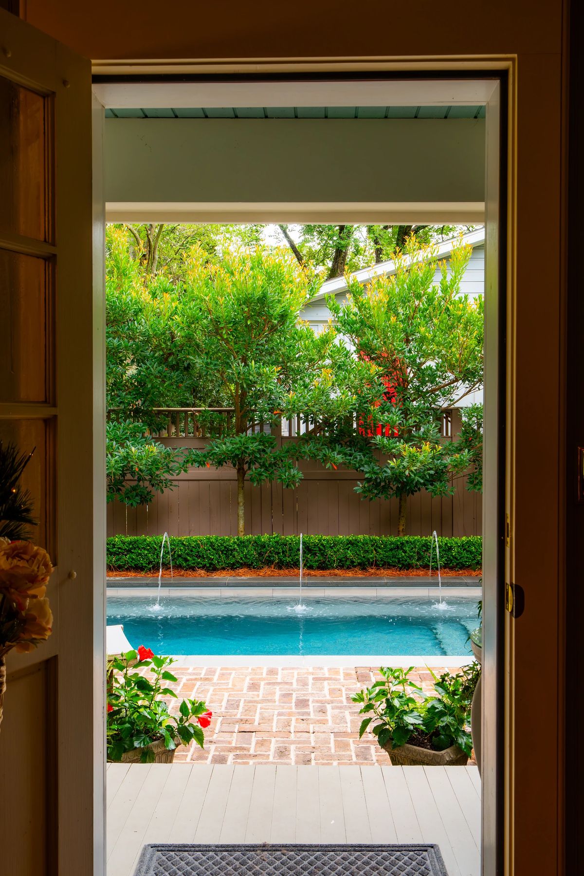 Exterior view with a pool, surrounded by greenery, shrubs, flowers, and a brick pathway.