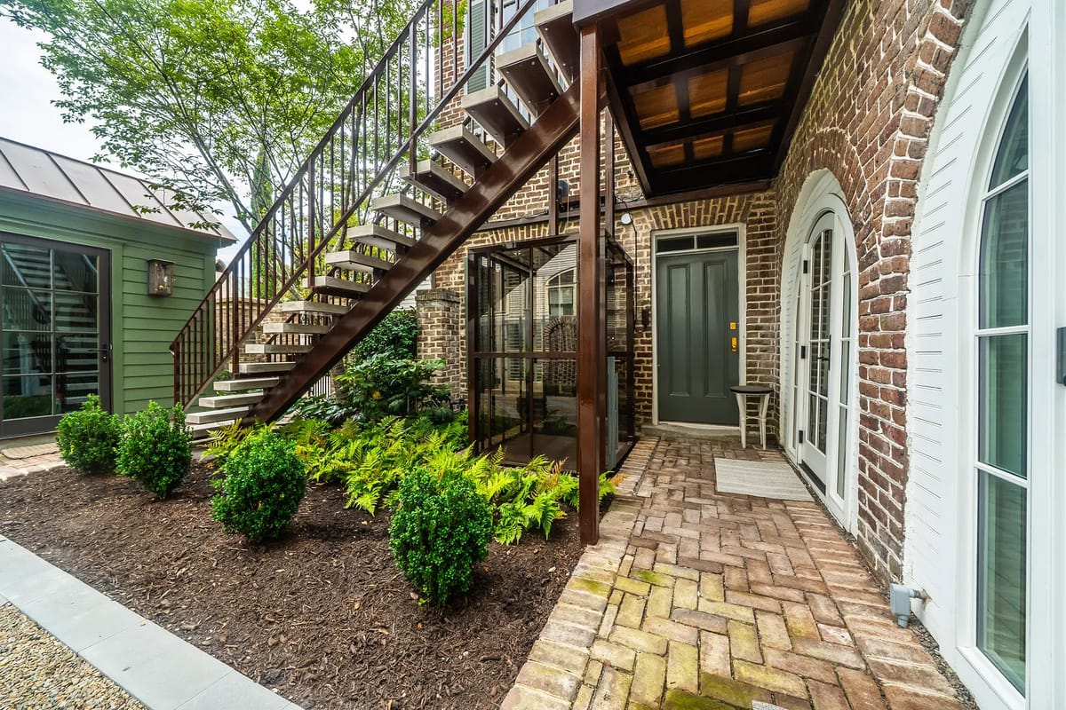 Exterior front with brick facade, iron staircase, glass enclosure, and landscaped area with ferns.