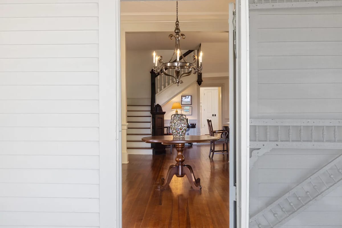 Foyer with round wooden table, vase, chandelier, staircase, and hardwood flooring.