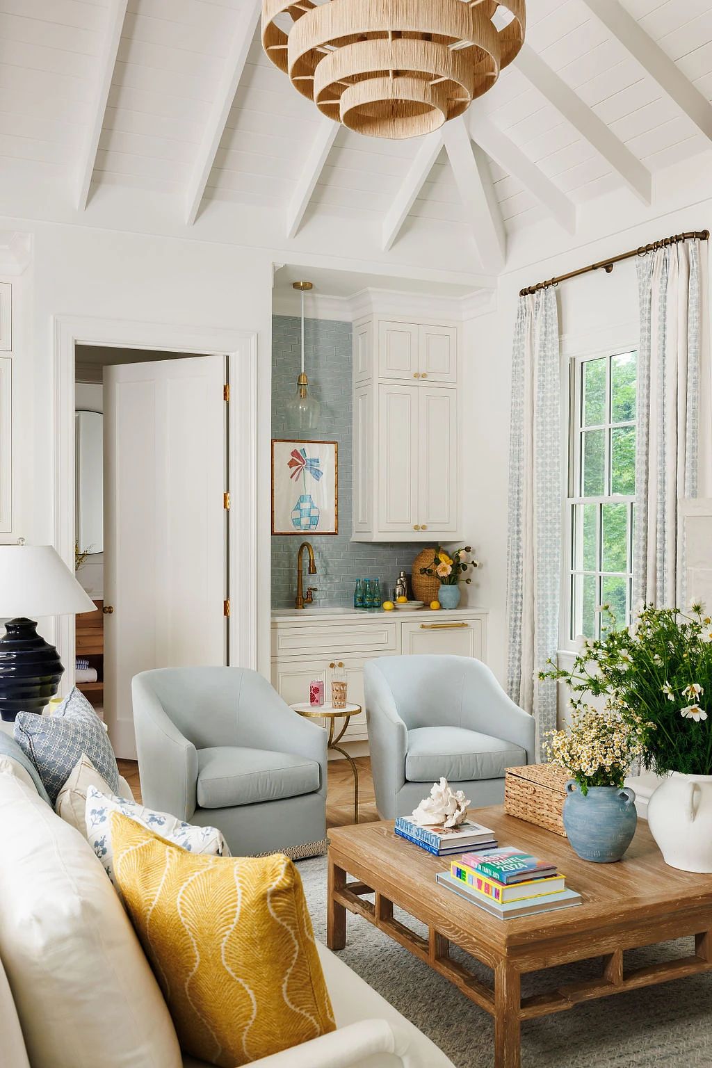Living room with white sofa, light blue armchairs, wooden coffee table, large window, and wooden chandelier.
