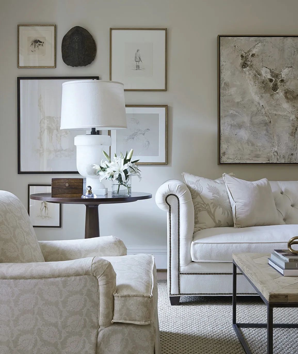 Living room with cream sofa, armchair, side table, coffee table, framed art, and neutral area rug.