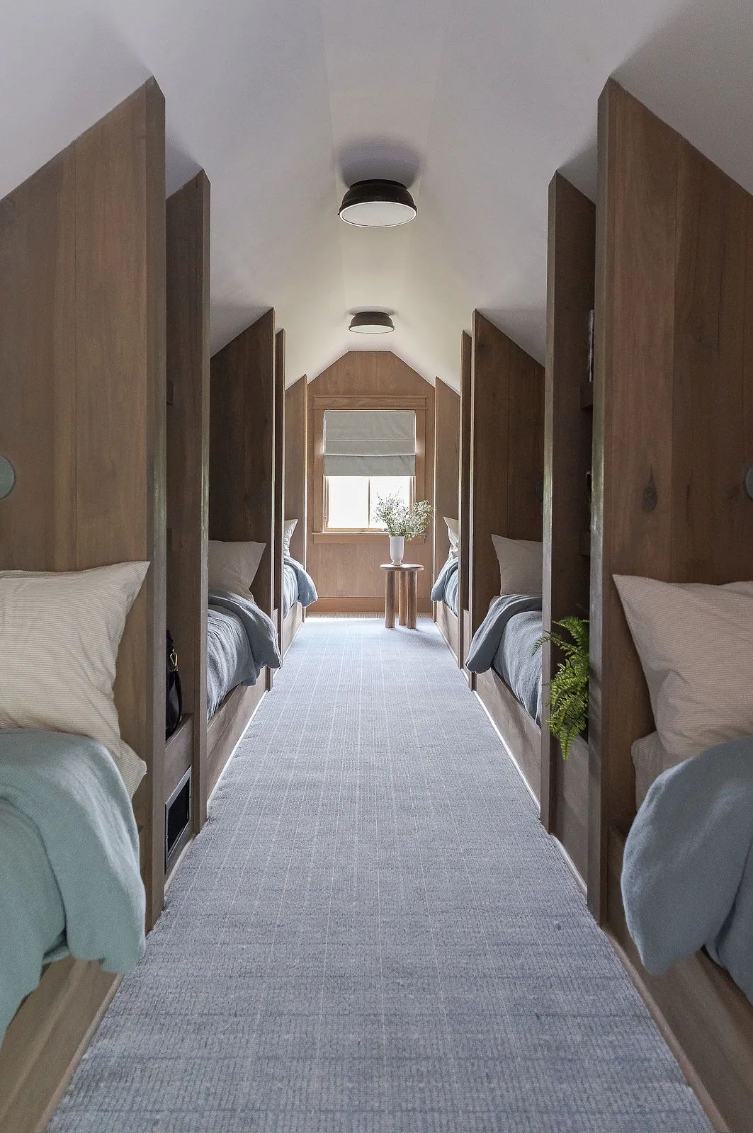 Bedroom with four sleeping areas, light blue blankets, nightstands, and a central window for natural light.