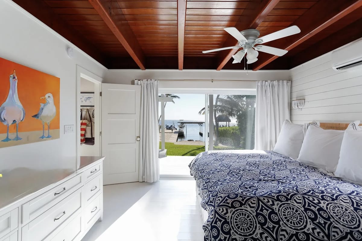 Bedroom with king-size bed, white nightstands, sliding glass door, and wooden beam ceiling.