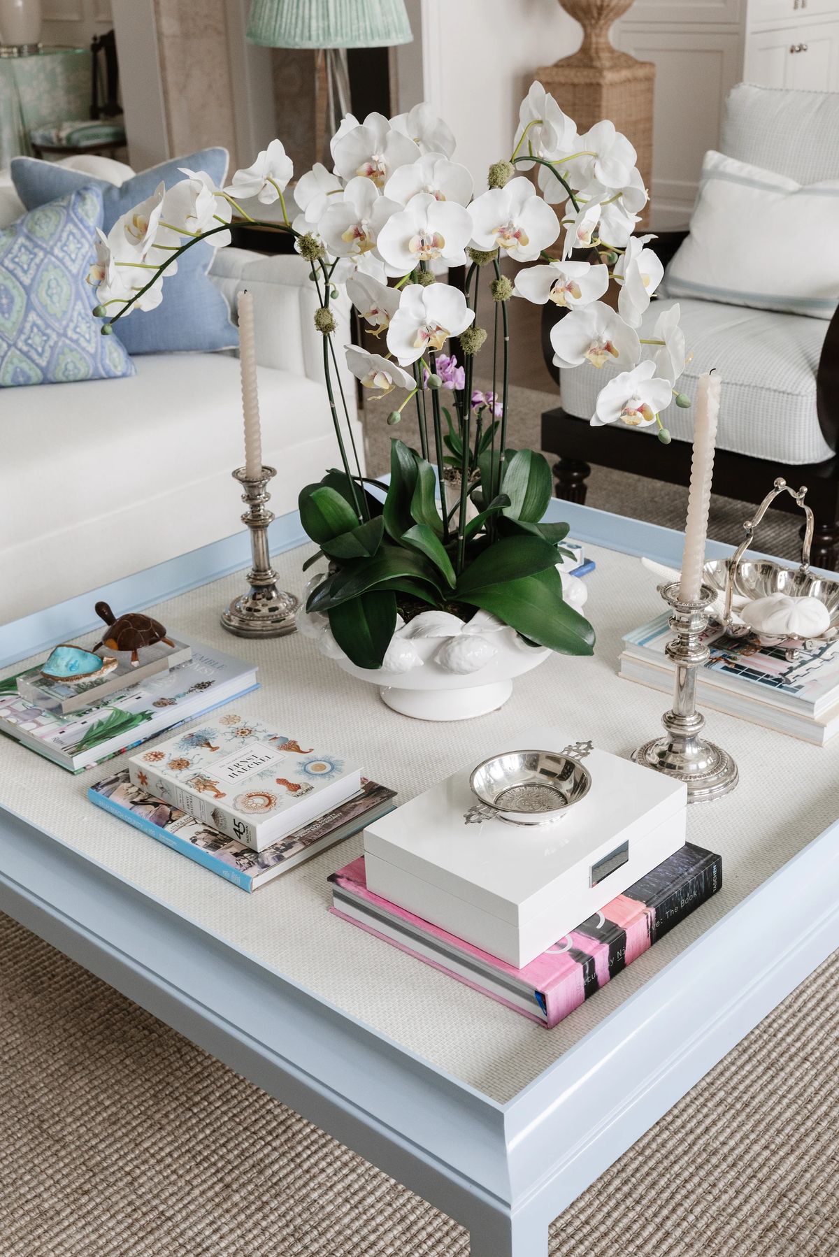 Living room with light blue coffee table, white sofa, orchids, candlesticks, and magazines.