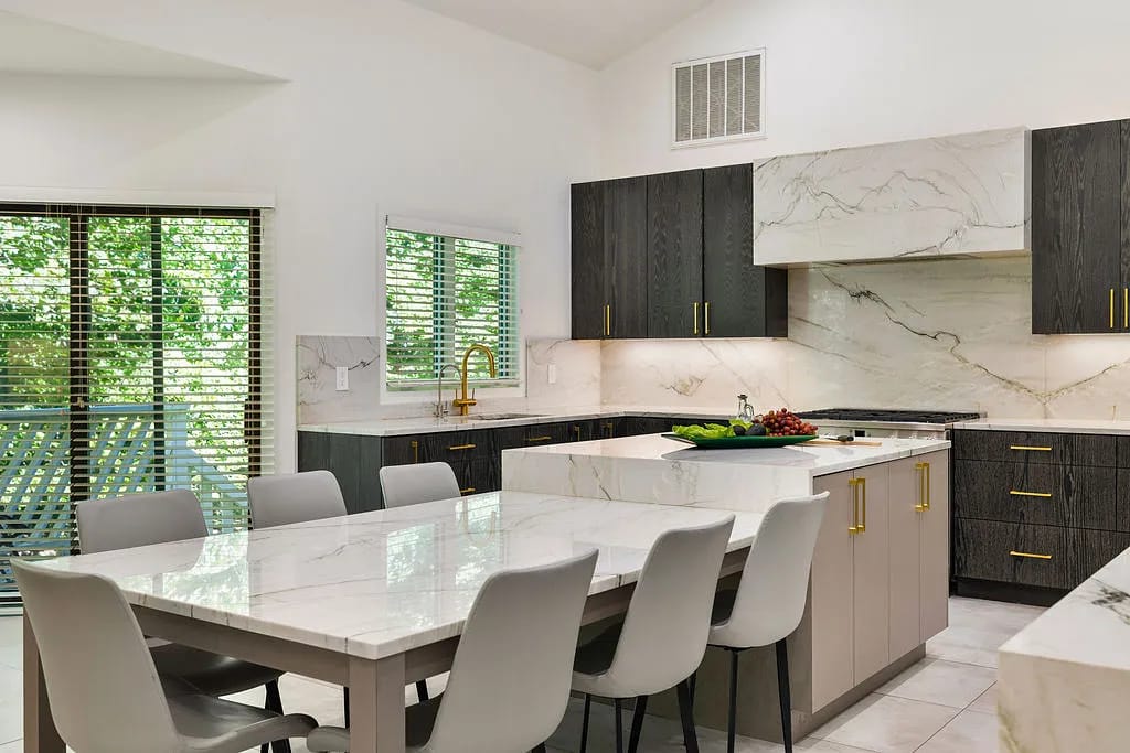 Kitchen with dark wood cabinets, marble countertops, island, dining table, and gray chairs with natural light from windows