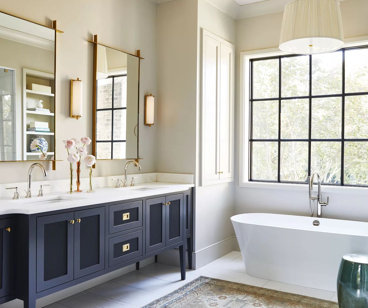 Bathroom with freestanding tub, dark blue vanity, dual mirrors, and window with natural light.