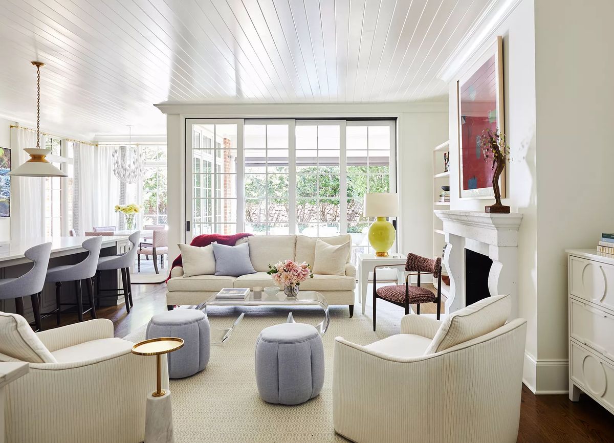 Living room with white sofa, gray ottomans, coffee table, area rug, fireplace, and large windows