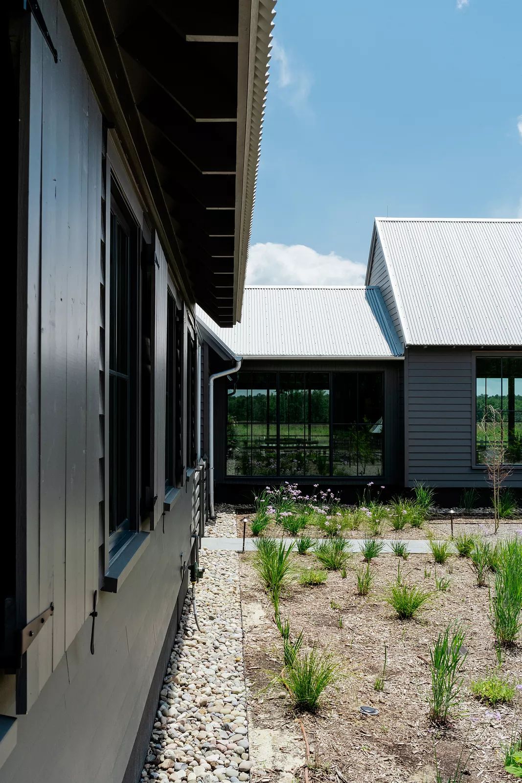 Exterior view of a grey building with stone path, landscaping, and metal roof.