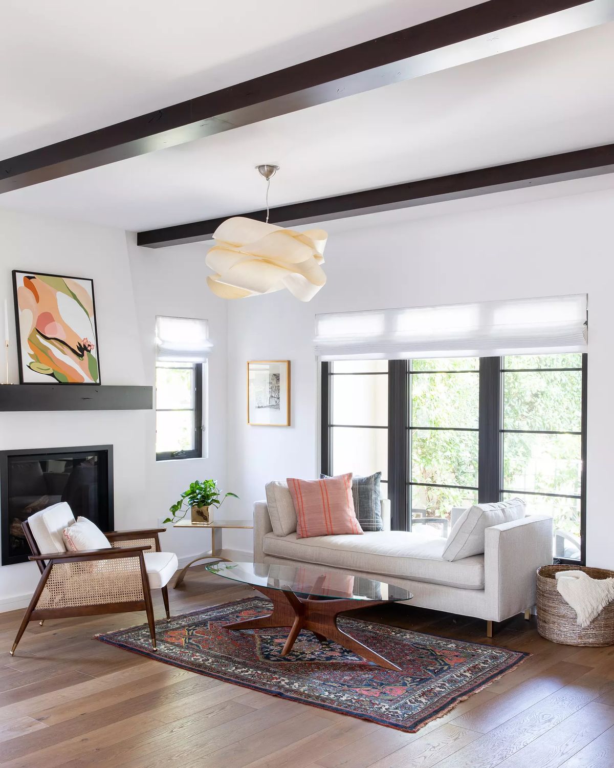 Living room with white sofa, patterned rug, wooden coffee table, large windows, black fireplace, and wall art