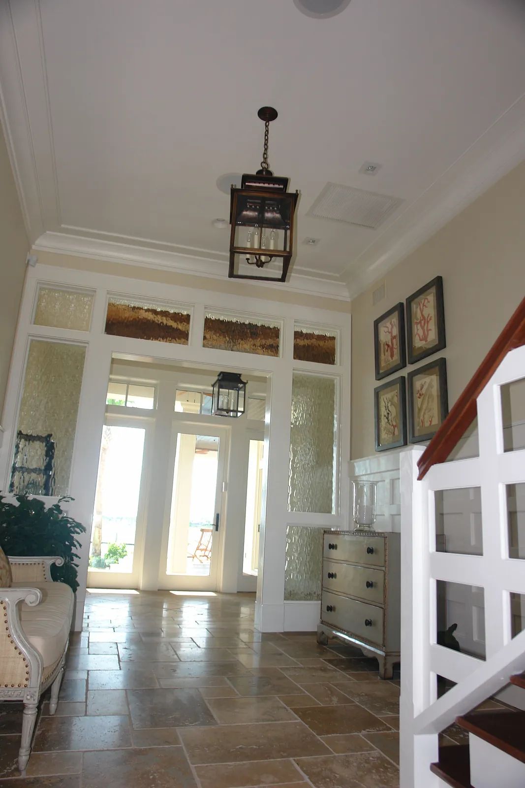 Foyer with staircase, console table, artwork, glass doors, and pendant light.