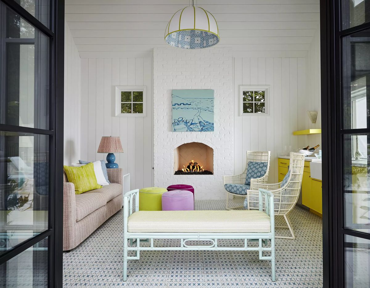 Living room with pink sofa, accent chairs, poufs, kitchenette, and white brick fireplace.