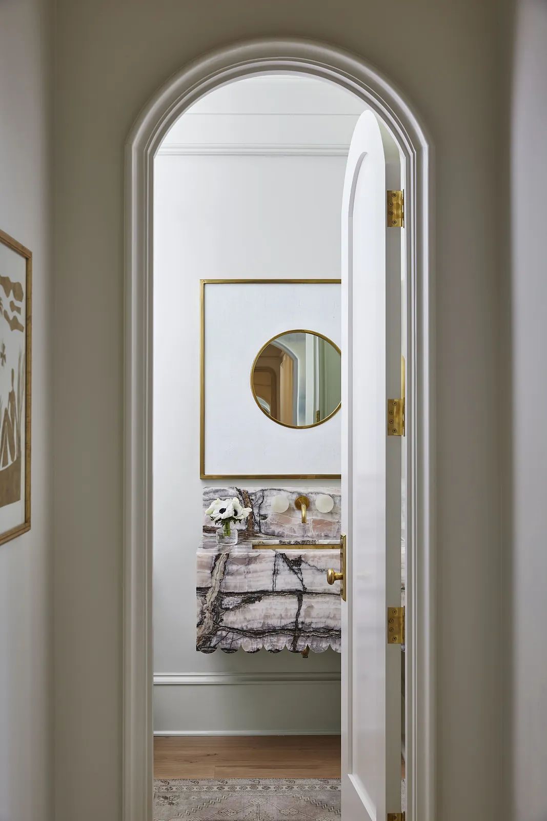 Powder room with marble counter, circular mirror, wall art, and patterned area rug.